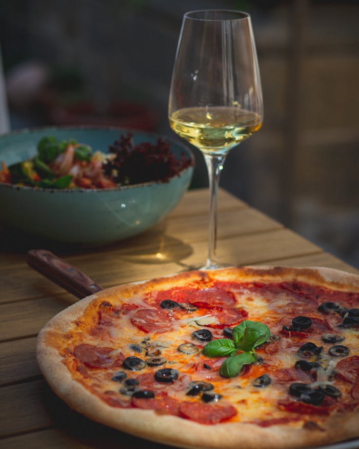 Tasty pepperoni pizza served with white wine outdoor, perfect for dining delight.